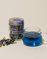 A jar of dried flowers and a cup of blue tea showcasing Single Origin Butterfly Pea, a fragrant herbal drink.
