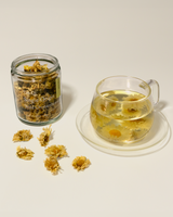 Wild Chrysanthemum tea in a glass cup beside a jar of dried flowers.