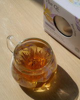 A glass teapot filled with Blue Lotus Flower Tea, showcasing the blooming whole flower against a soft wooden background.