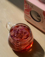 Cup of Shangri-la Rose! tea featuring vibrant rose petals against a wooden background.