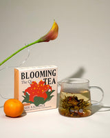 Inner Radiance Blooming Tea box with brewed tea in glass and an orange, showcasing a blooming tea experience.