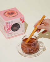 Iconic Bloom Trio set: A hand stirring Shangri-La Rose tea in a clear cup beside the colorful packaging.