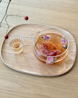 Floral Tea Tasting featuring a glass teapot with blooming flowers and a tasting cup on a wooden tray.