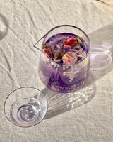 NYBG x Flower Tea Tasting Experience with a pitcher of floral tea and a glass cup on a linen tablecloth.