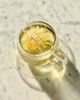 Glass cups & saucers (2) featuring tea with a flower in a glass cup on a marble surface.