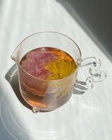 Bloom glass teapot (The Qi x SLJ) filled with flower tea showcasing vibrant colors and a unique design.