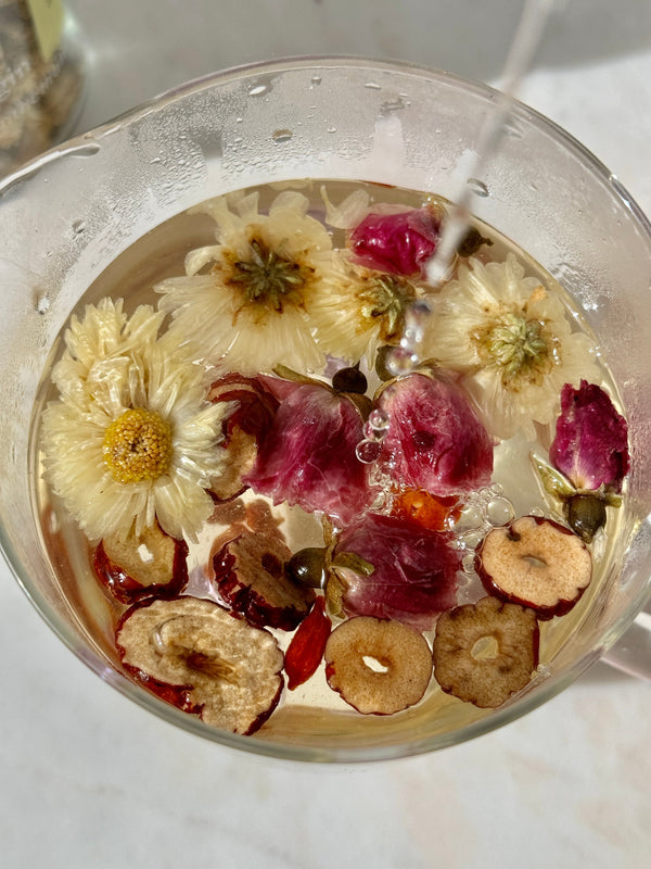 How to Naturally Balance Hormones with Flower Teas in a glass of herbal tea with dried flowers and fruits.