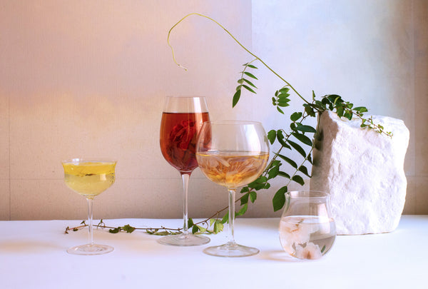 4 elegant glasses of flower teas on a table, showcasing vibrant colors and a decorative branch.